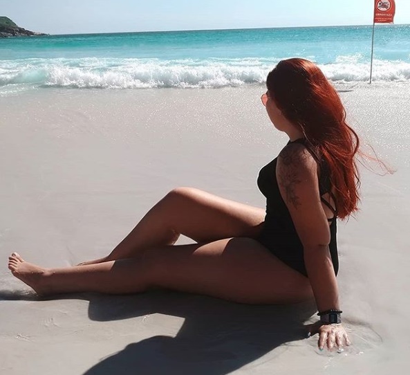 MUlher sentada na areia da praia olhando para o mar