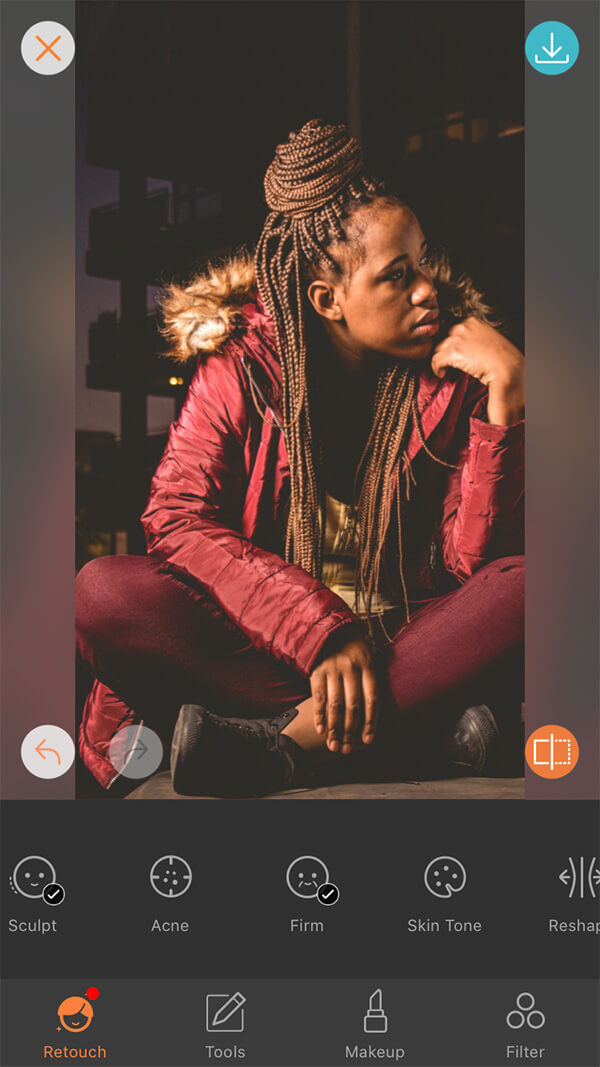 woman with braids in red jacket and pants sits in front of dark background