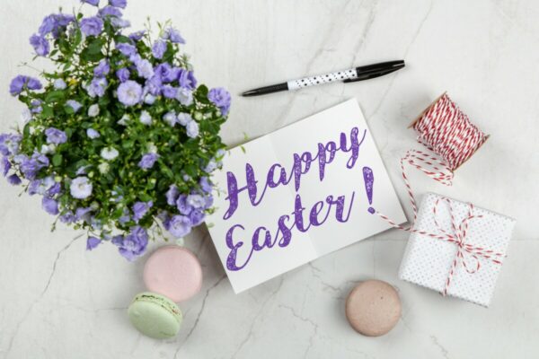 Foto de uma flor, presentes, macarons e um bilhete escrito "Happy Easter" que sifnigica Feliz Páscoa