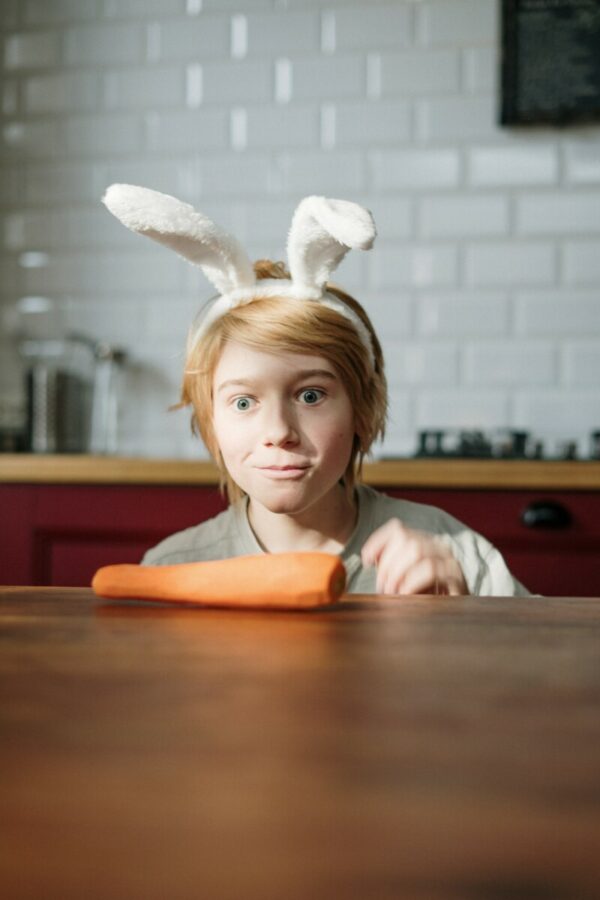 Foto de uma pessoa com orelhas de coelho olhando para uma cenoura