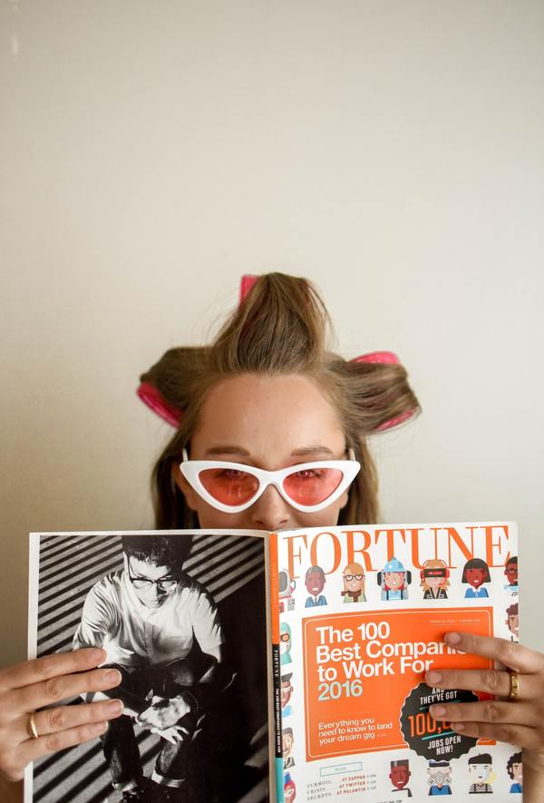 mujer con tubos en la cabeza, lentes de sol y una revista