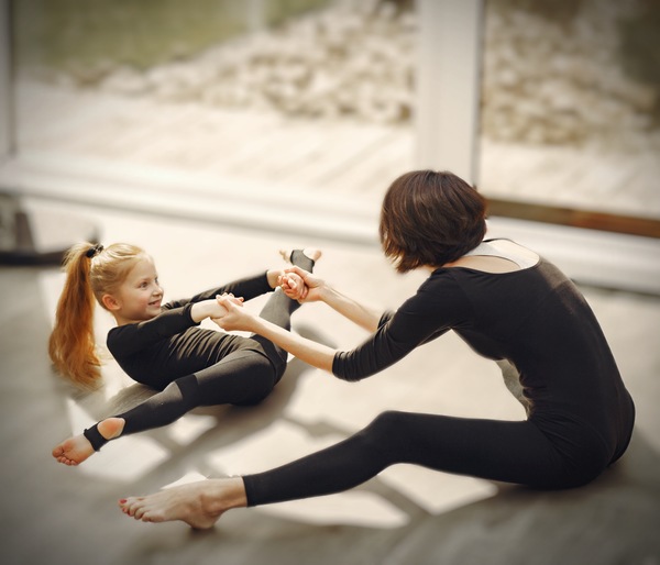 Foto de mamá practicando ballet o gimnasia con su hija. Ambas están vestidas con un payasito negro y están haciendo estiramientos.
