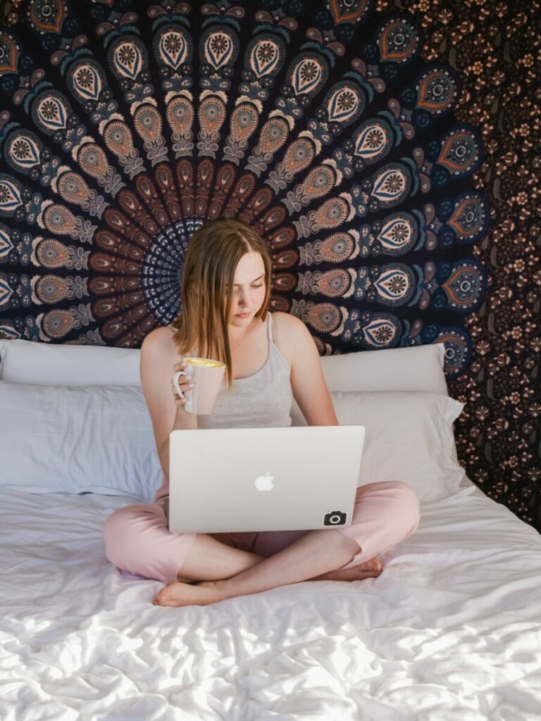 foto de uma mulher na cama usando o computador e bebendo café
