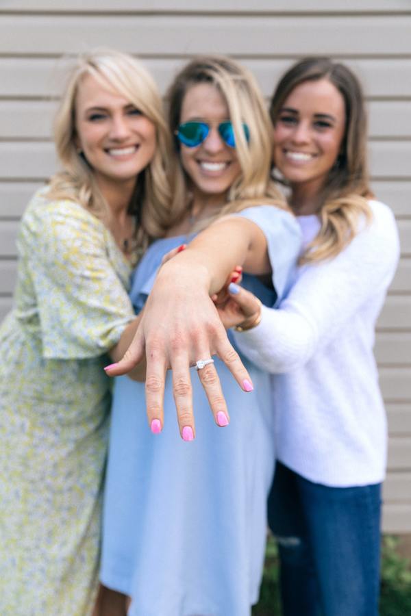 woman showing off her engagement ring while two friends hug her