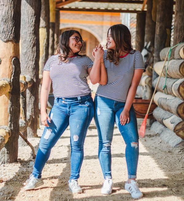 two women wearing jeans and striped t-shirts holding hands