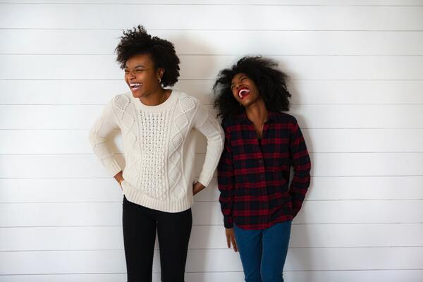 two women standing in front of a white wall laughing
