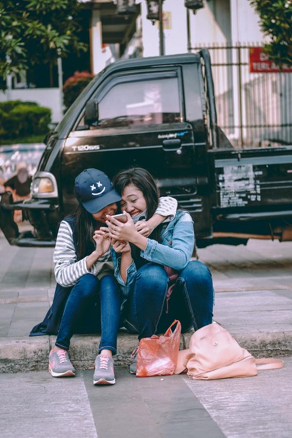 two girls seated on the sidewalk hugging