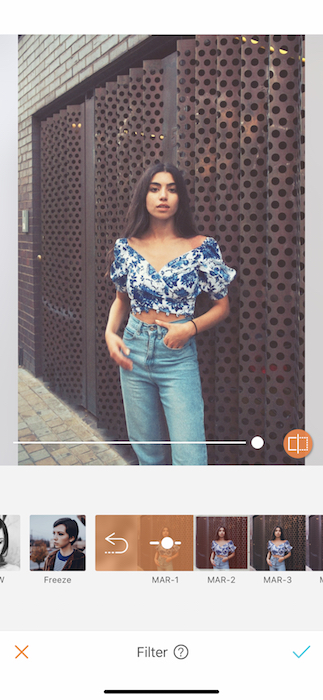 Kim Kardashian lookalike in blue jeans and floral top standing in front of metal wall