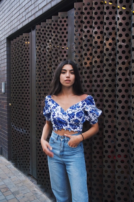 Kim Kardashian lookalike in blue jeans and floral top standing in front of metal wall