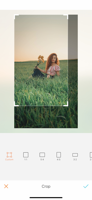 Picture of a ginger woman holding yellow flowers sitting in grass at the open field being edited by AirBrush with the Crop Tool