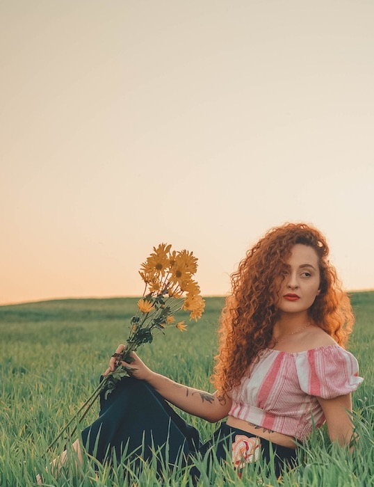 Picture of a ginger woman holding yellow flowers sitting in grass at the open field