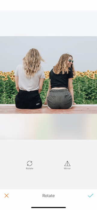 Picture of two girl friends sitting and looking at a sunflower field being edited by AirBrush with the Rotate Tool