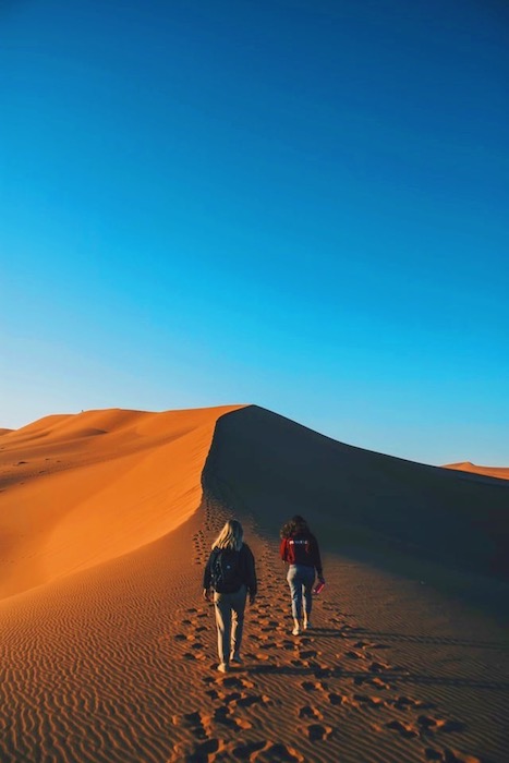 two women walking on a sand dune