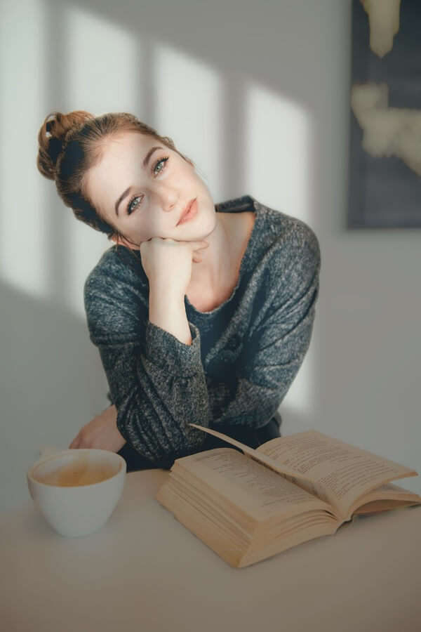 Mujer con un libro abierto sobre la mesa y una taza de café.