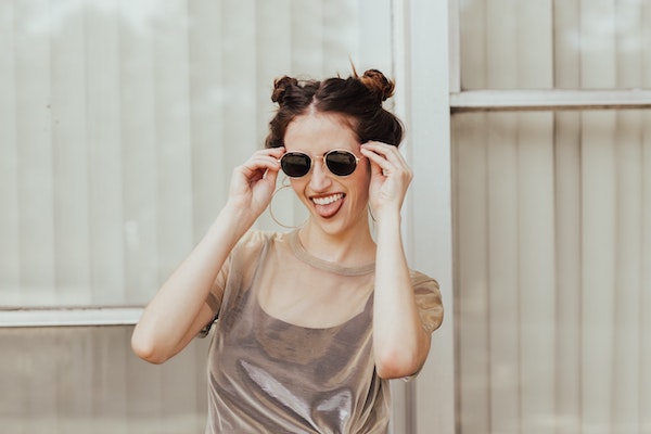 laughing woman holding sunglasses up to her face against light background