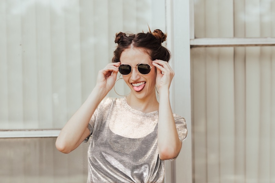 laughing woman holding sunglasses up to her face against light background