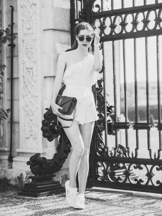 black and white photo of a woman in a white romper standing in front of a black gate