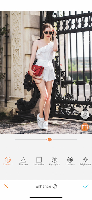 woman in a white romper holding a red purse in front of a black gate