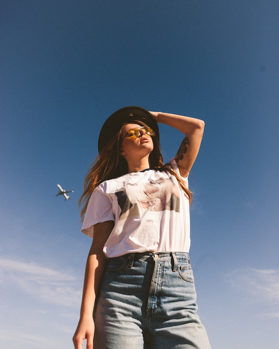 woman wearing white t-shirt and jeans stands in front of a blue sky