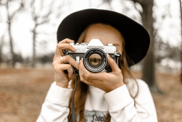 woman wearing a black hat takes a photo with a vintage camera
