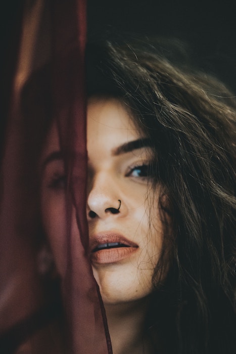 closeup photo of a woman with dark hair and nose ring, half her face is covered by dark cloth fabric