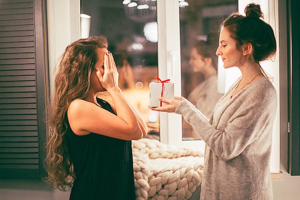 woman covers her eyes while another woman surprises her with a gift