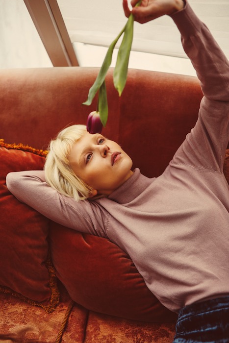 woman wearing a pink sweater lying on a sofa holding a flower