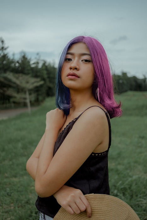 woman with purple and blue hair standing in green field