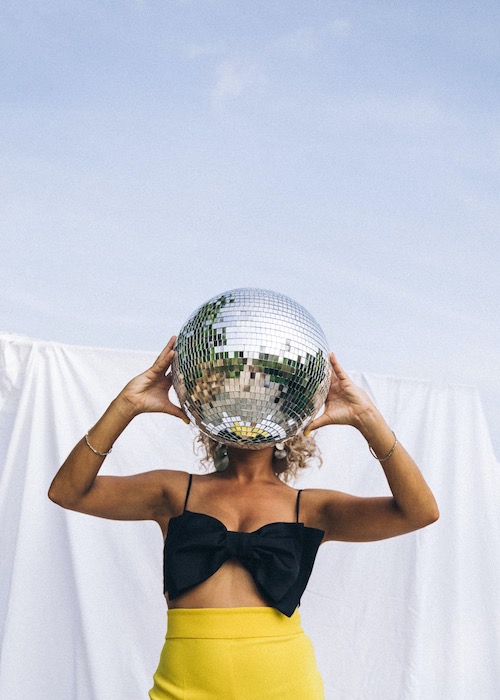 woman in yellow skirt holding disco ball with sky background