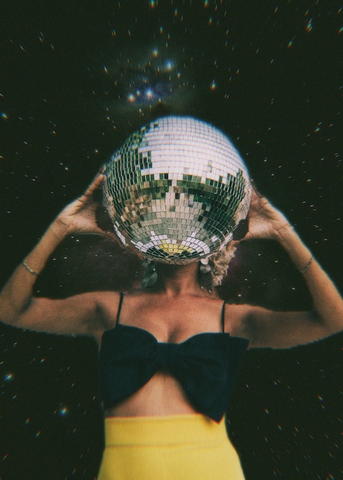 woman in yellow skirt holding disco ball in front of starry background