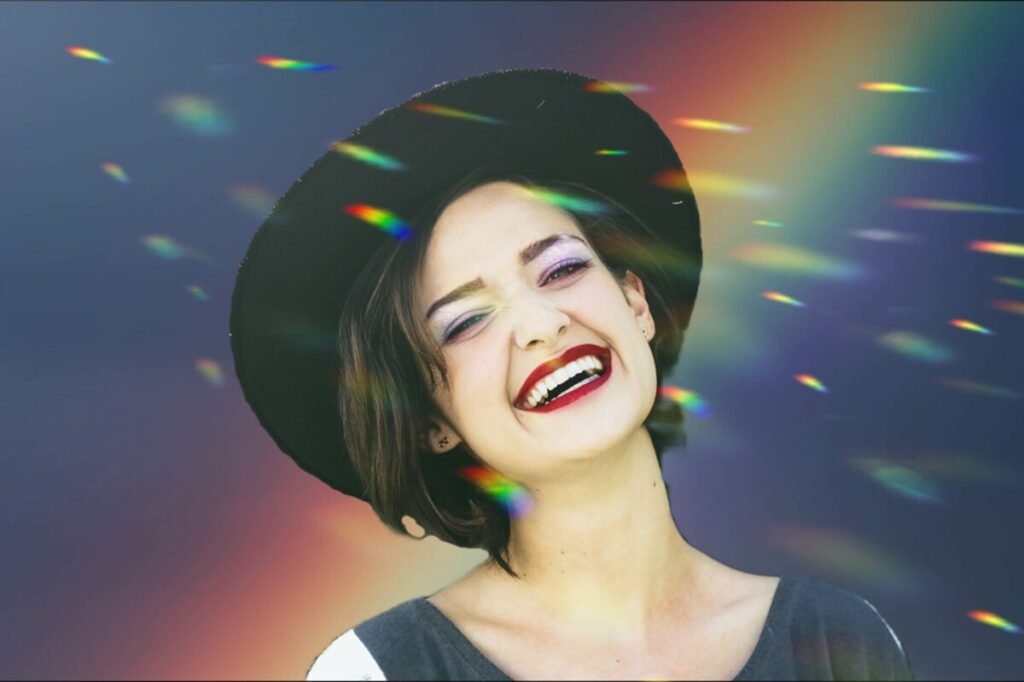 Pride edit of laughing woman wearing a hat in front of a rainbow background