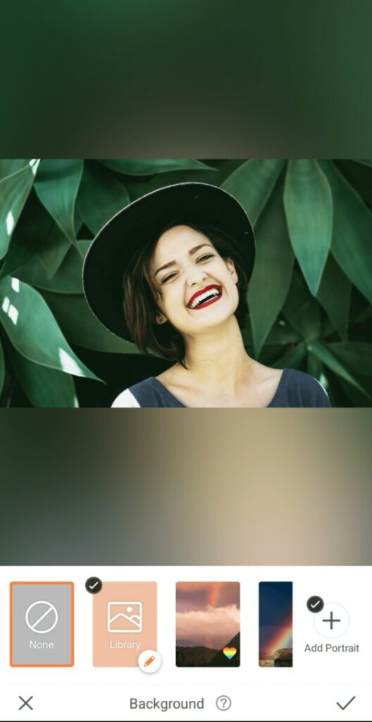 laughing woman wearing a hat in front of a leafy background