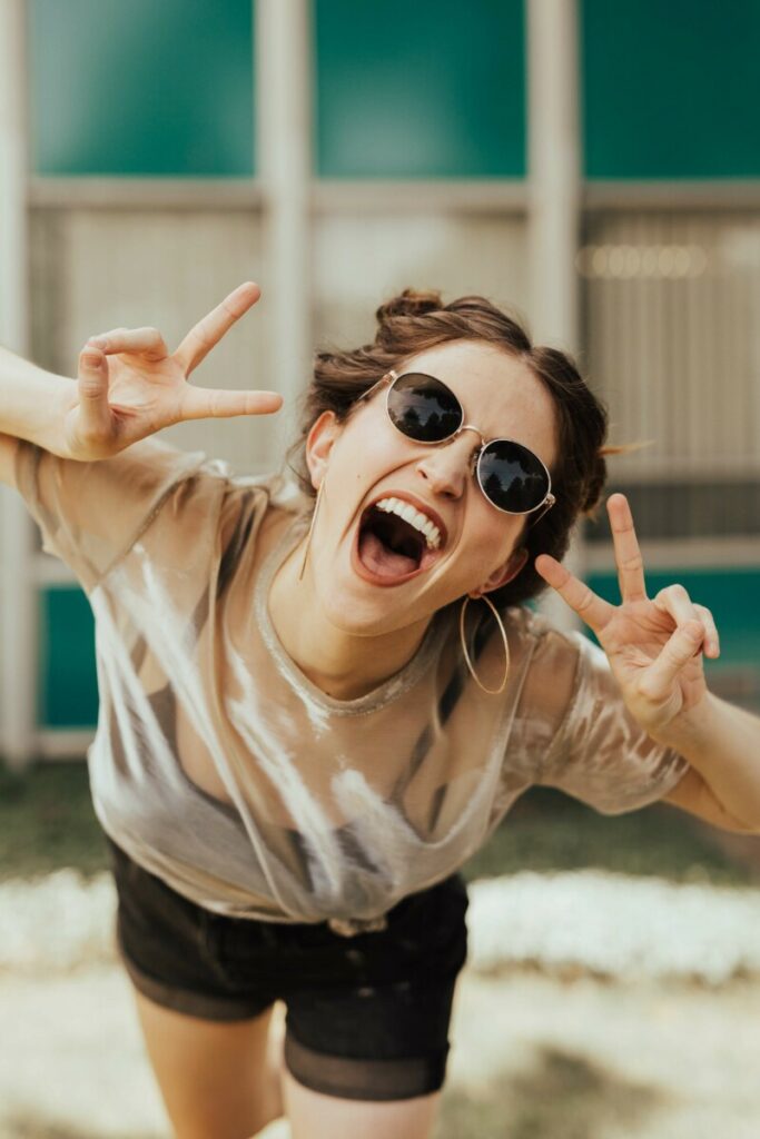 laughing woman in white top and sunglasses making the peace sign