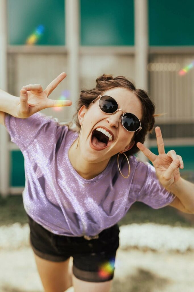Pride Month edit of laughing woman in purple top and sunglasses making the peace sign