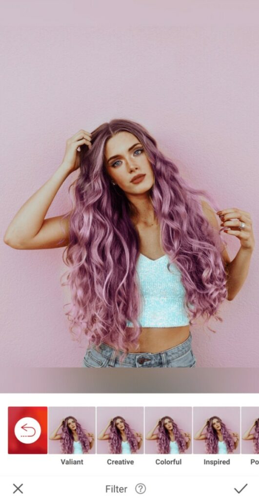 Pride edit of woman with purple hair in a white top stands in front of a pink wall