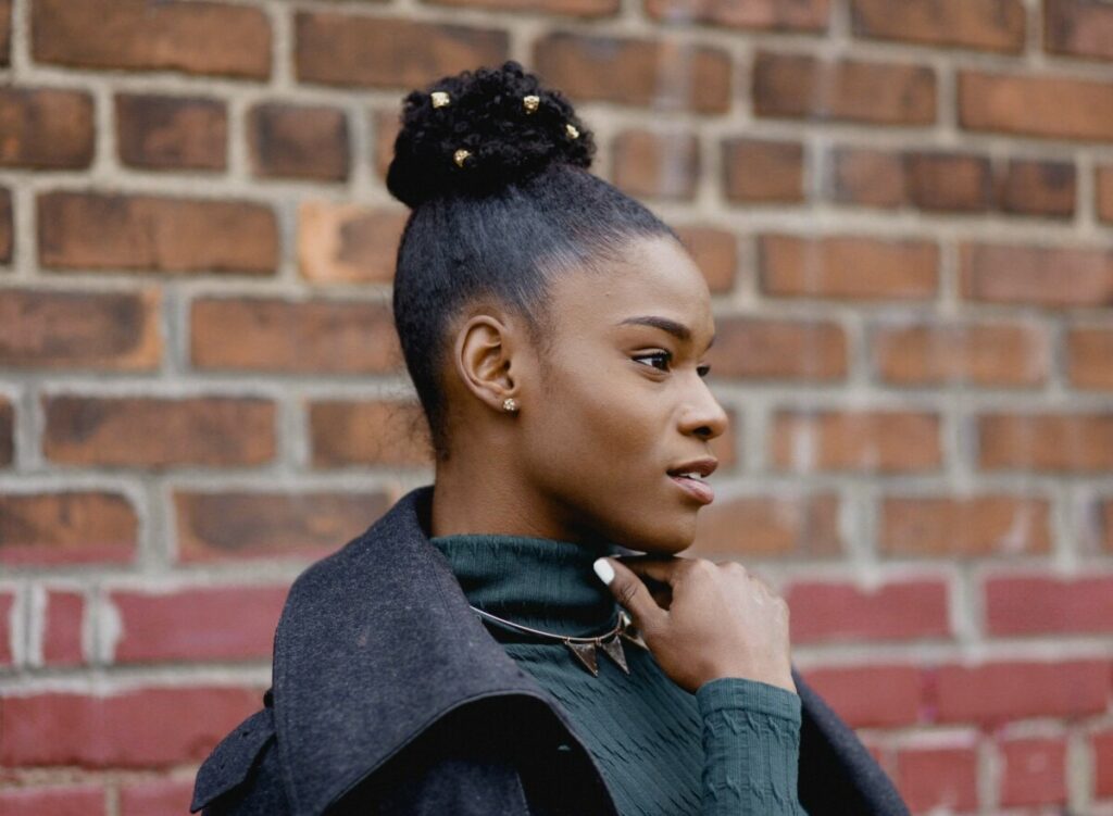 profile of black woman wearing a jacket standing in front of a red brick wall