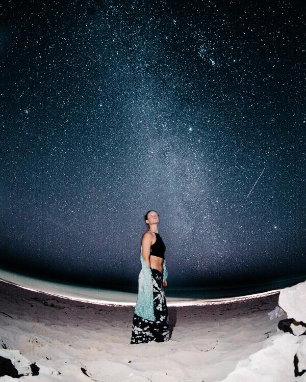 Garota de blusa preta e saia estampada com um céu estrelado ao fundo