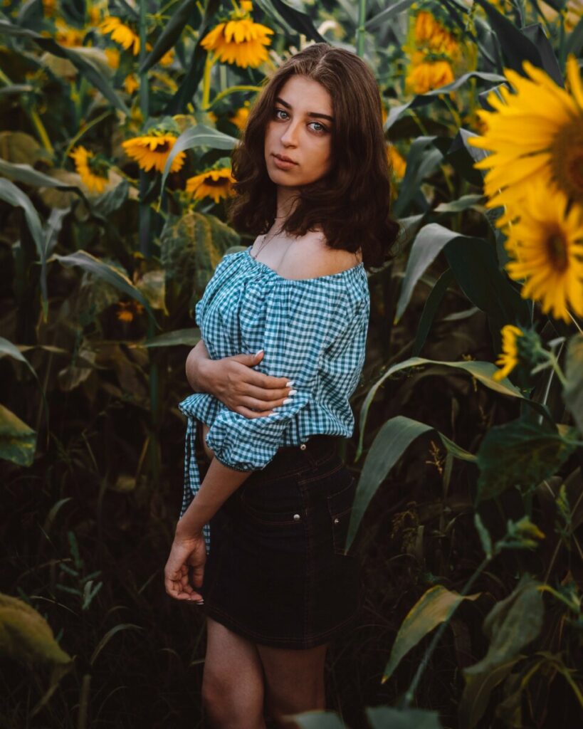 girl in blue checkered top standing in sunflower field