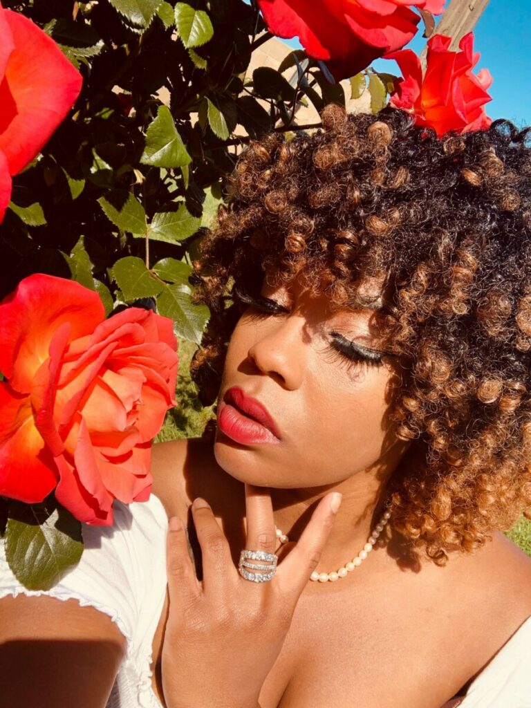 closeup of woman with curly hair posing beside bright red flowers