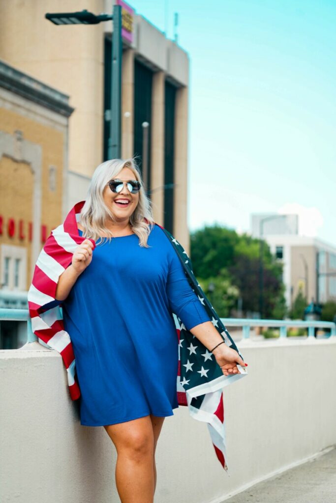 woman in blue dress and American flag celebrates July 4th
