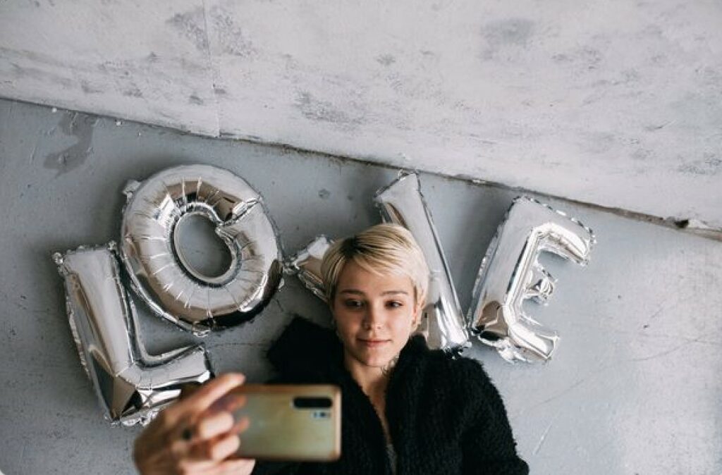 woman takes selfie on top of LOVE balloons