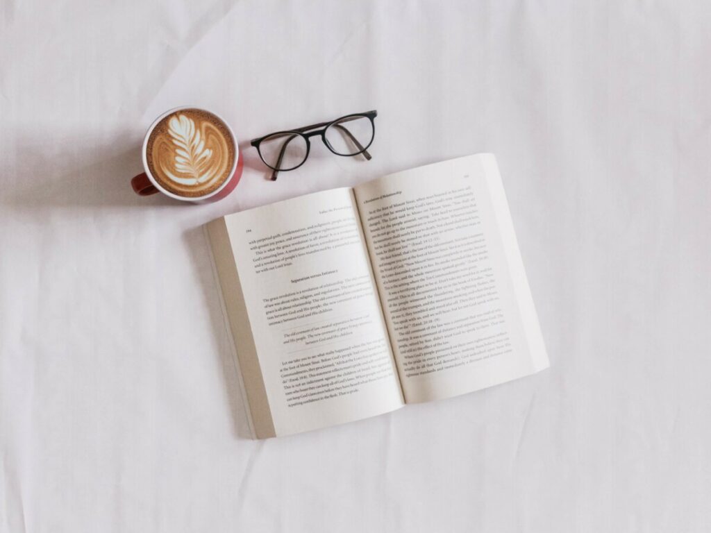 flat lay of an open book with coffee and reading glasses