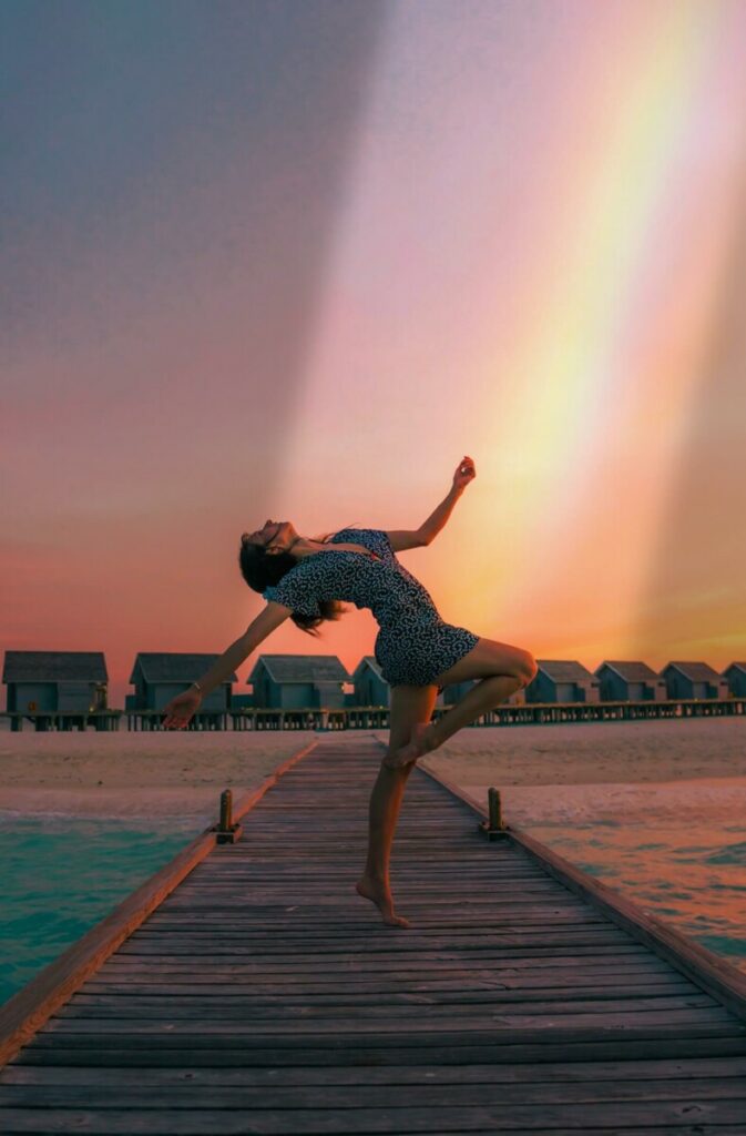 woman posing on a jetty with a rainbow in the sky 