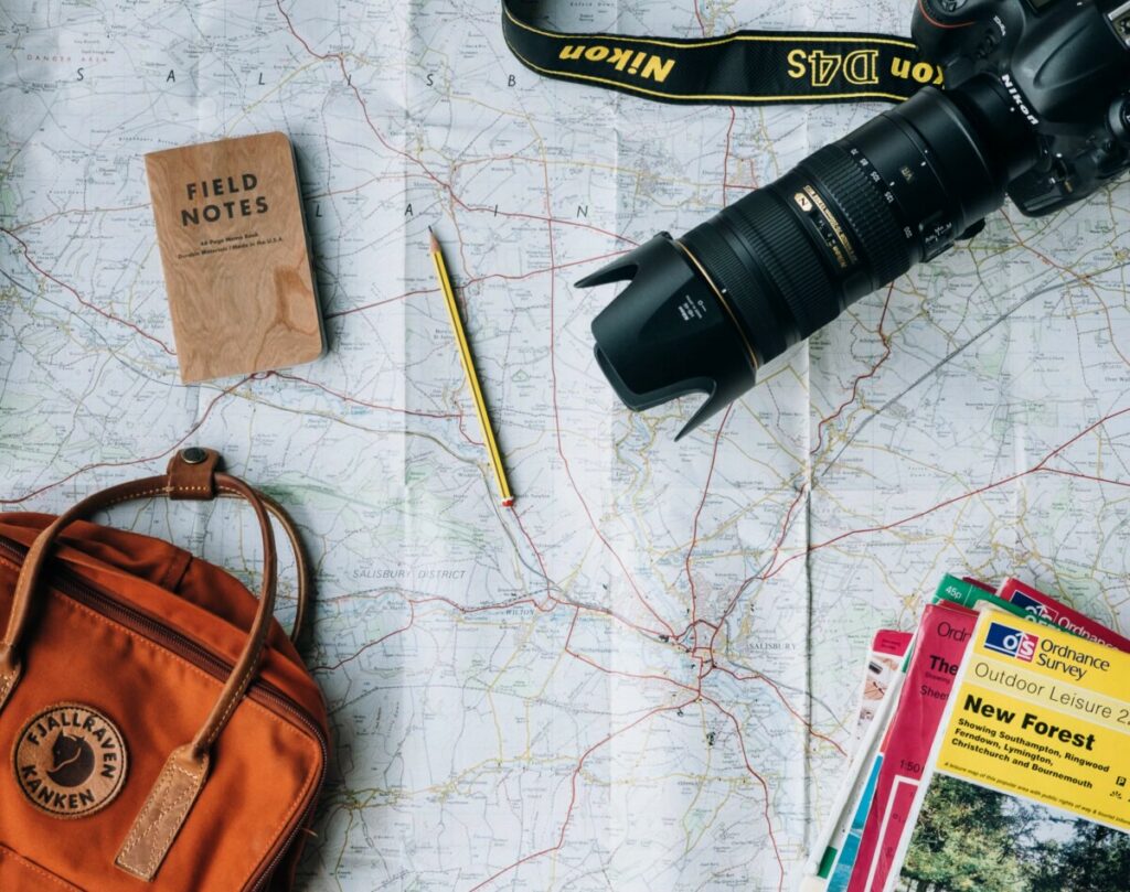 travel flat lay featuring a camera, backpack, notepad and map