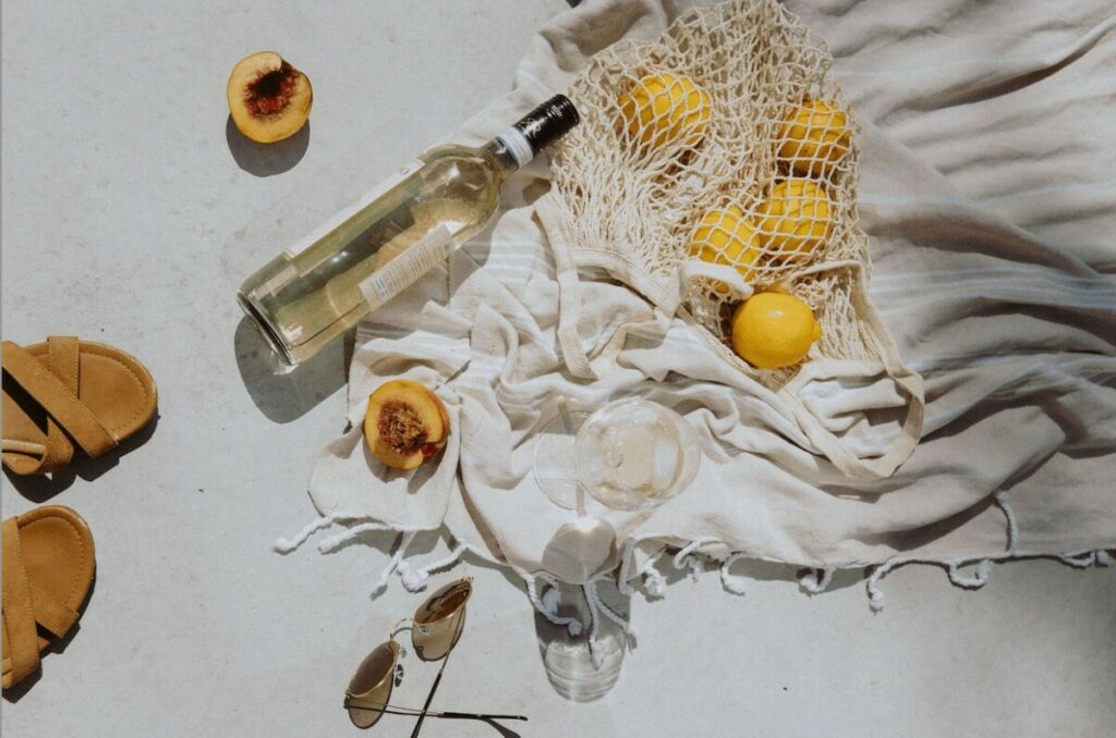 overhead photo of a bottle of wine, fruit, sunglasses and a blanket