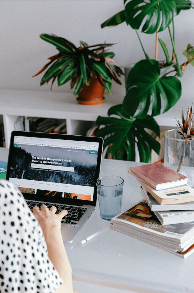 woman using a laptop on a desk with books and plants